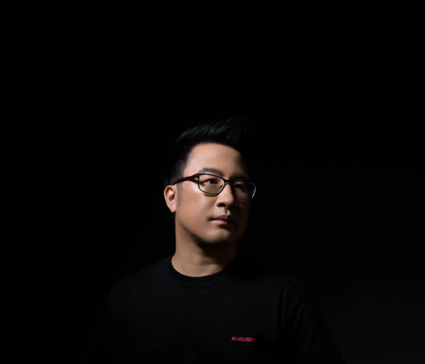 Portrait of a man wearing glasses and a black shirt against a dark background.
