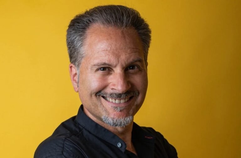 Smiling middle-aged man with gray hair and a goatee against a solid yellow background.