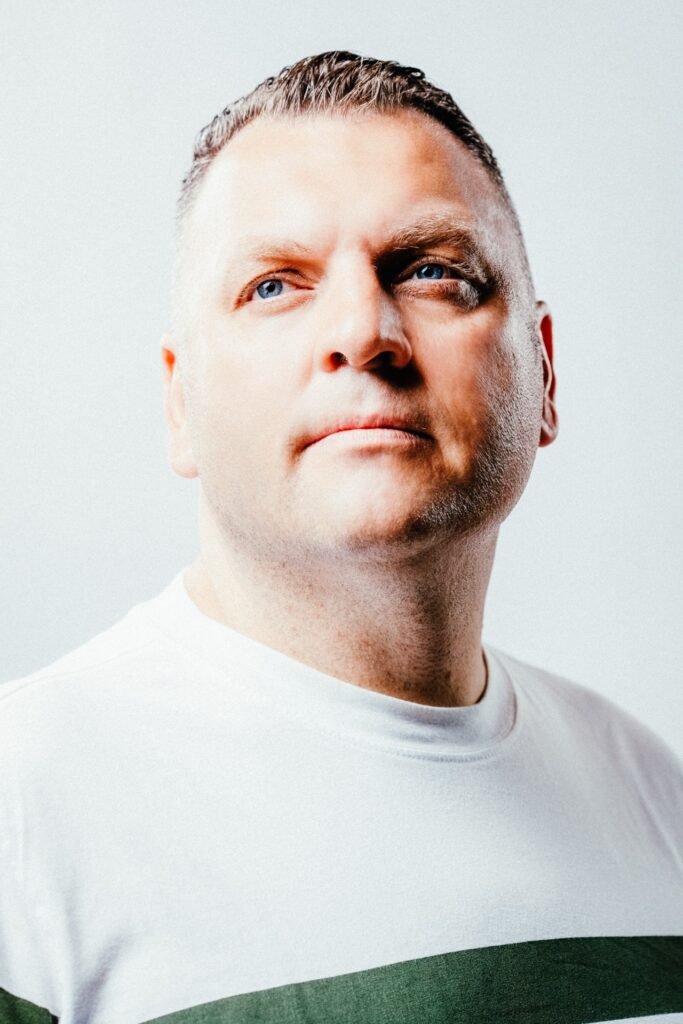 Close-up of a man’s face, partially cropped, wearing a white shirt with a green stripe against a pale background